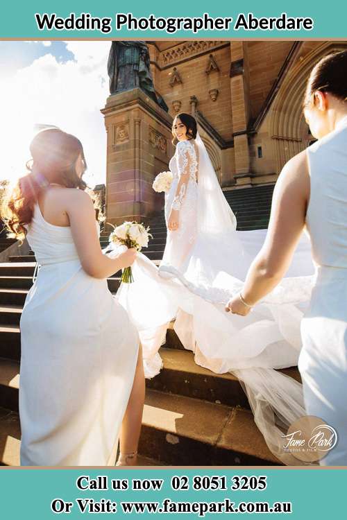 Photo of the Bride smiling while her bridesmaid holding the tail of her wedding gown outside the church Aberdare NSW 2325