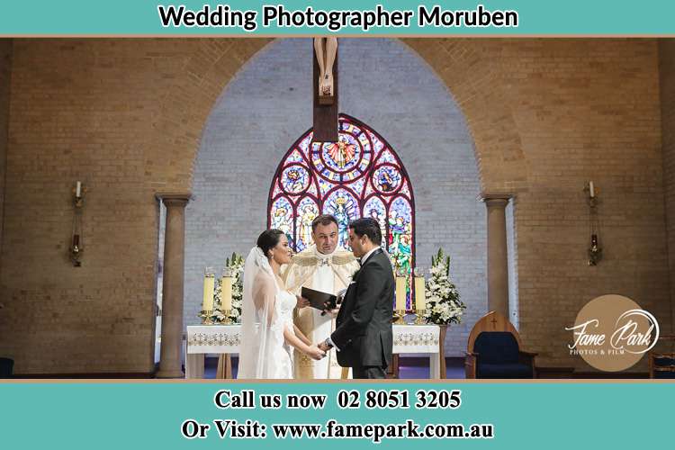 Photo of the Bride and the Groom at the altar with the priest at wedding ceremony Moruben NSW 2325